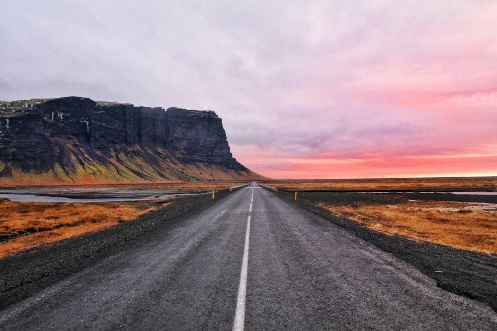 Empty road running toward a cliff under a pink sky in Iceland
