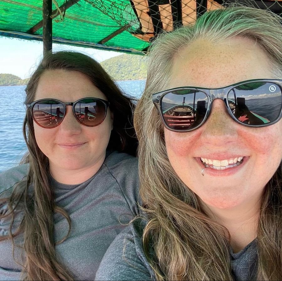 Mariya and Sam in sunglasses taking a selfie on a boat, with green islands behind them