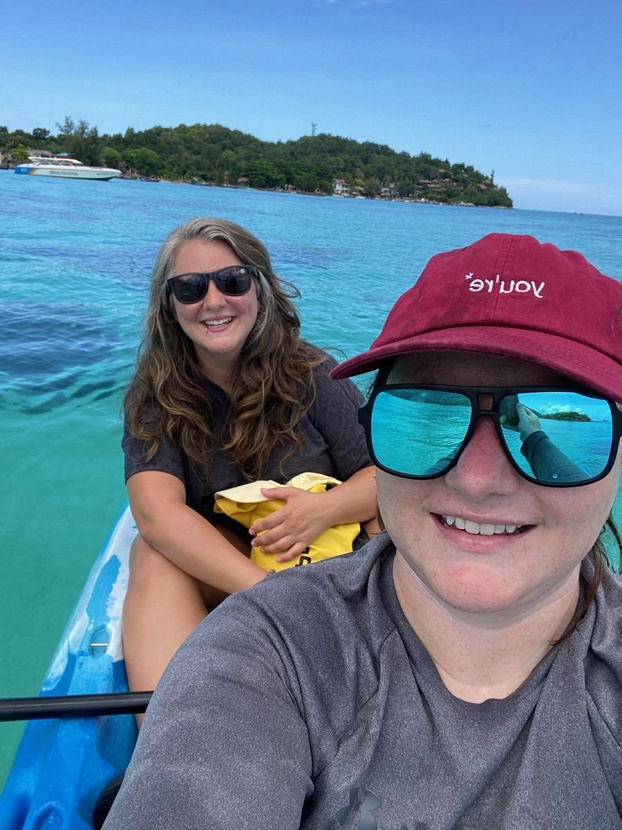 Mariya and Sam smiling in a kayak on clear turquoise water near a green island